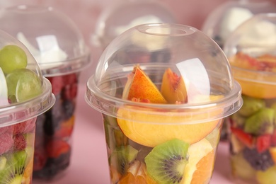 Photo of Fresh tasty fruit salad in plastic cups on pink table, closeup