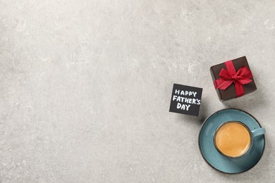 Photo of Card with phrase Happy Father's Day, gift box and cup of aromatic coffee on light grey background, flat lay. Space for text