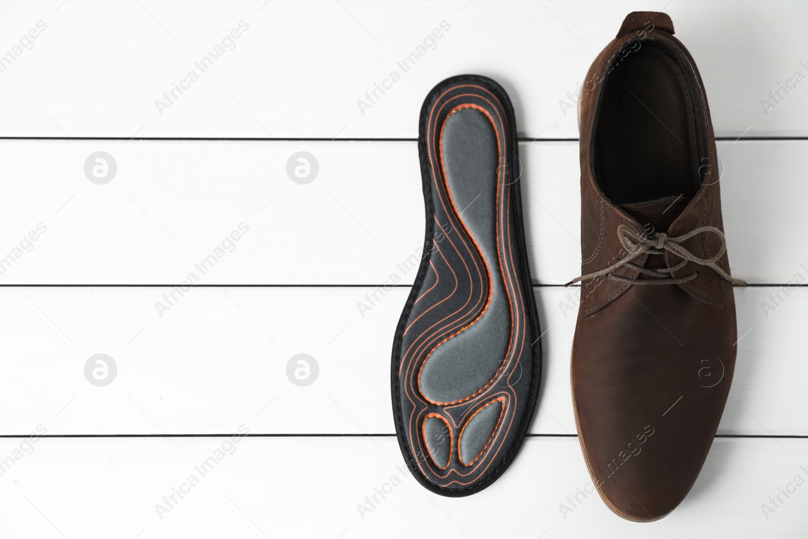 Photo of Orthopedic insole near shoe on white wooden floor, flat lay. Space for text