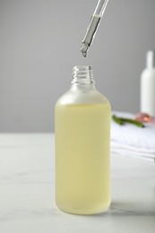 Photo of Dripping hydrophilic oil into bottle on white table, closeup
