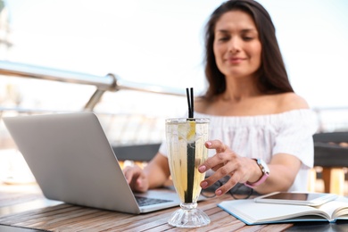Beautiful woman with refreshing drink and laptop at outdoor cafe