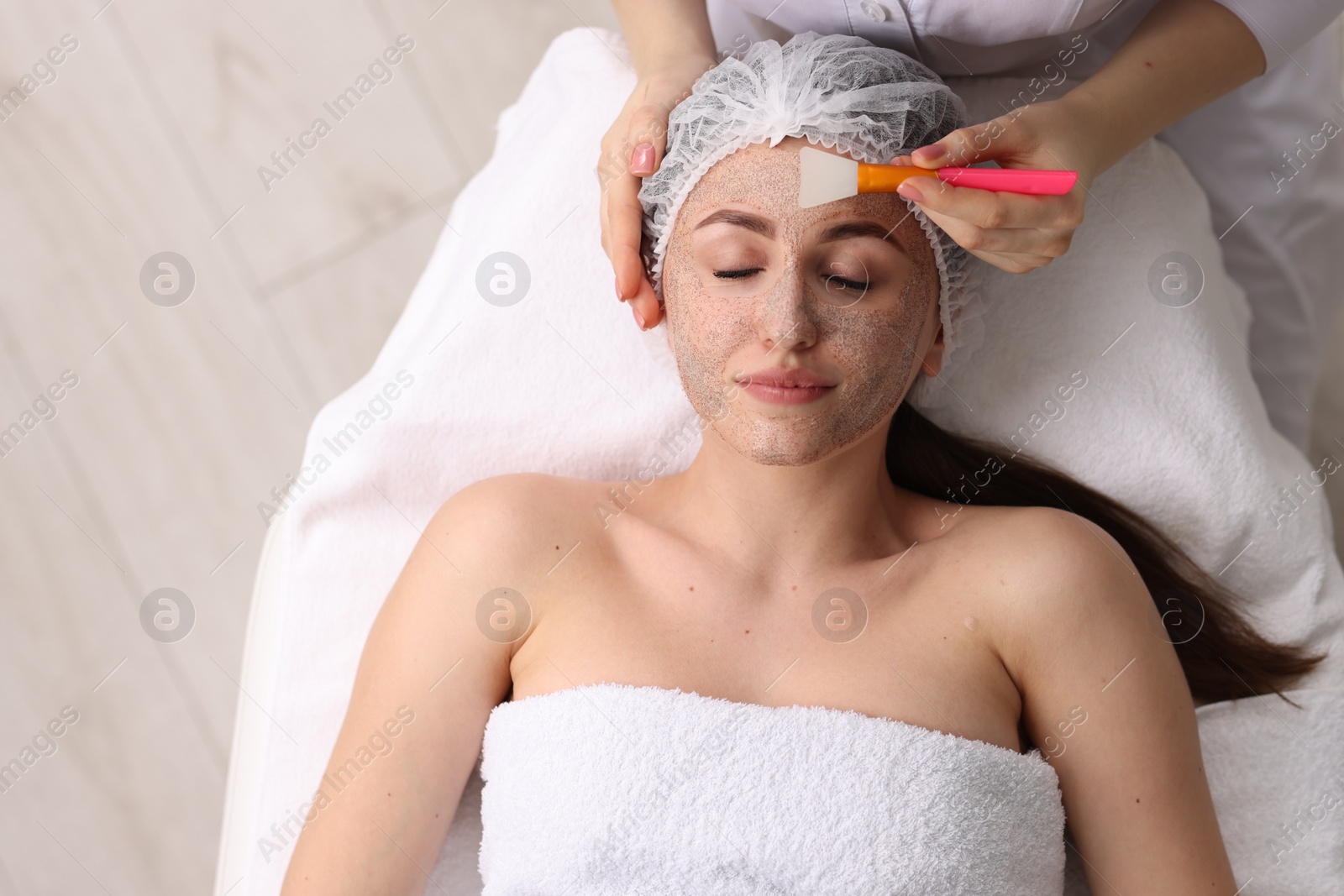 Photo of Cosmetologist applying mask on woman's face in clinic, top view