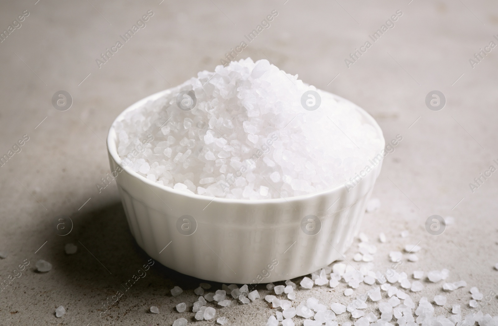 Photo of Bowl with salt on light grey table, closeup