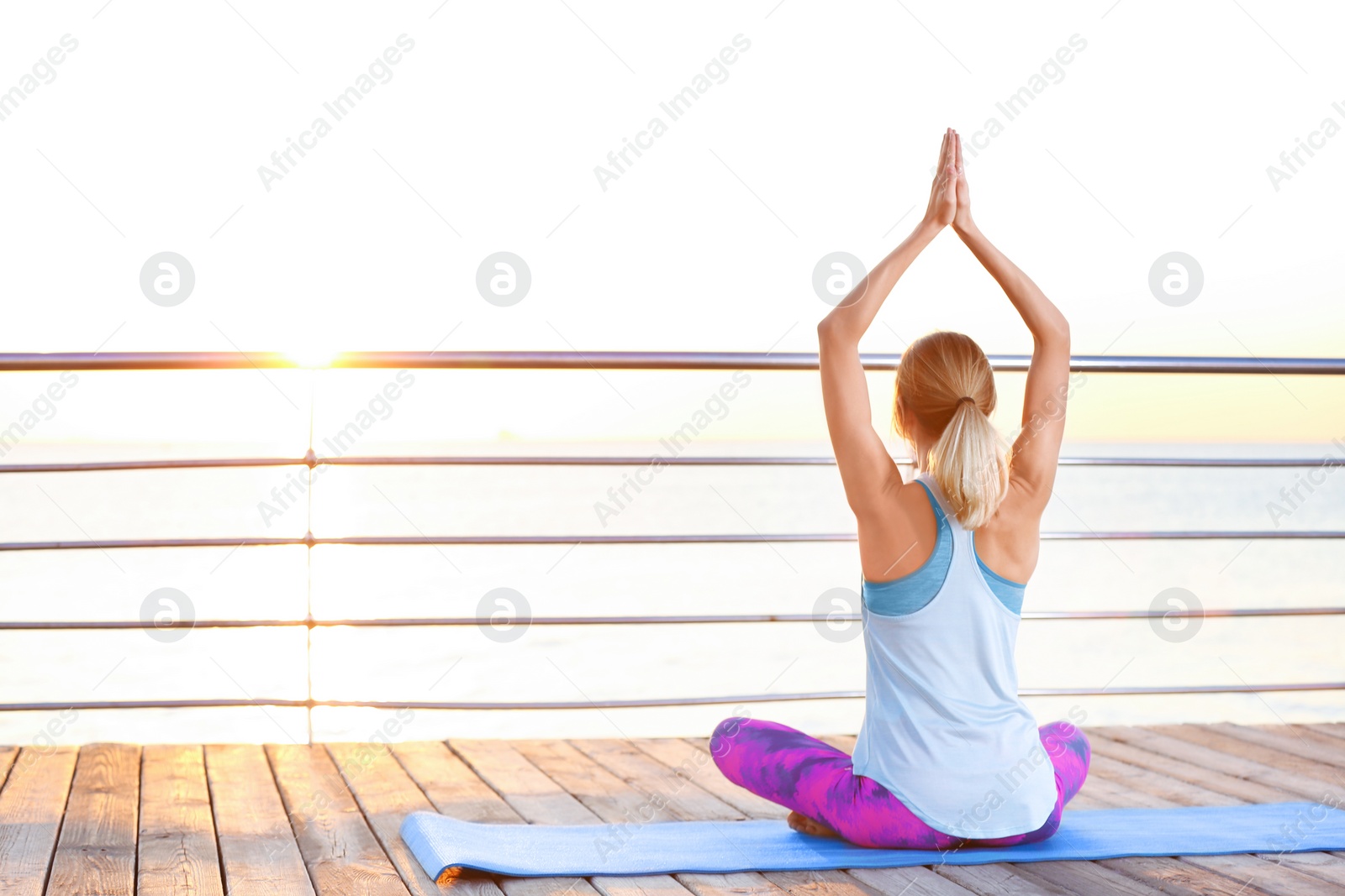 Photo of Young woman doing yoga exercises on pier in morning