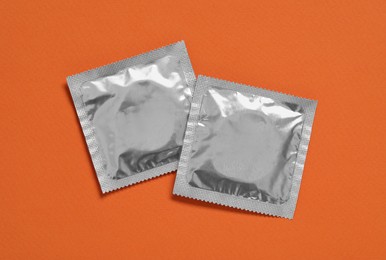 Photo of Condom packages on orange background, flat lay. Safe sex