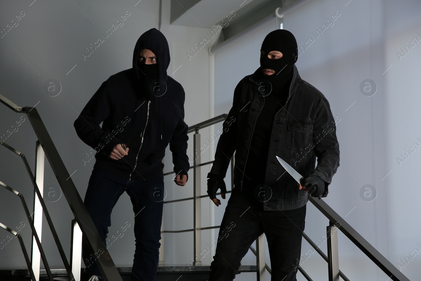 Photo of Men in masks with knives on stairs indoors. Dangerous criminals