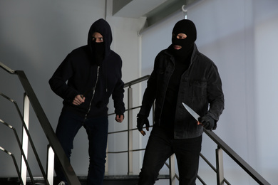 Men in masks with knives on stairs indoors. Dangerous criminals