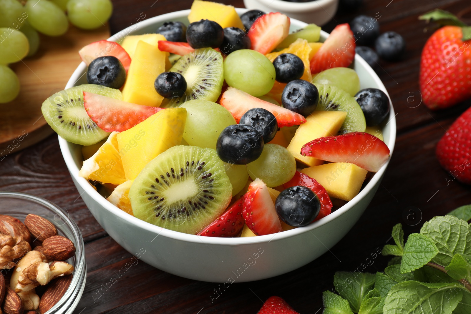 Photo of Tasty fruit salad in bowl and ingredients on wooden table, closeup