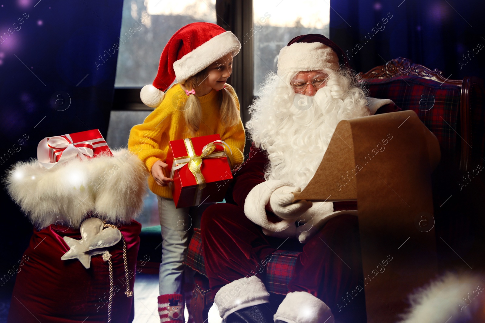 Photo of Little girl with Christmas gift near Santa Claus indoors