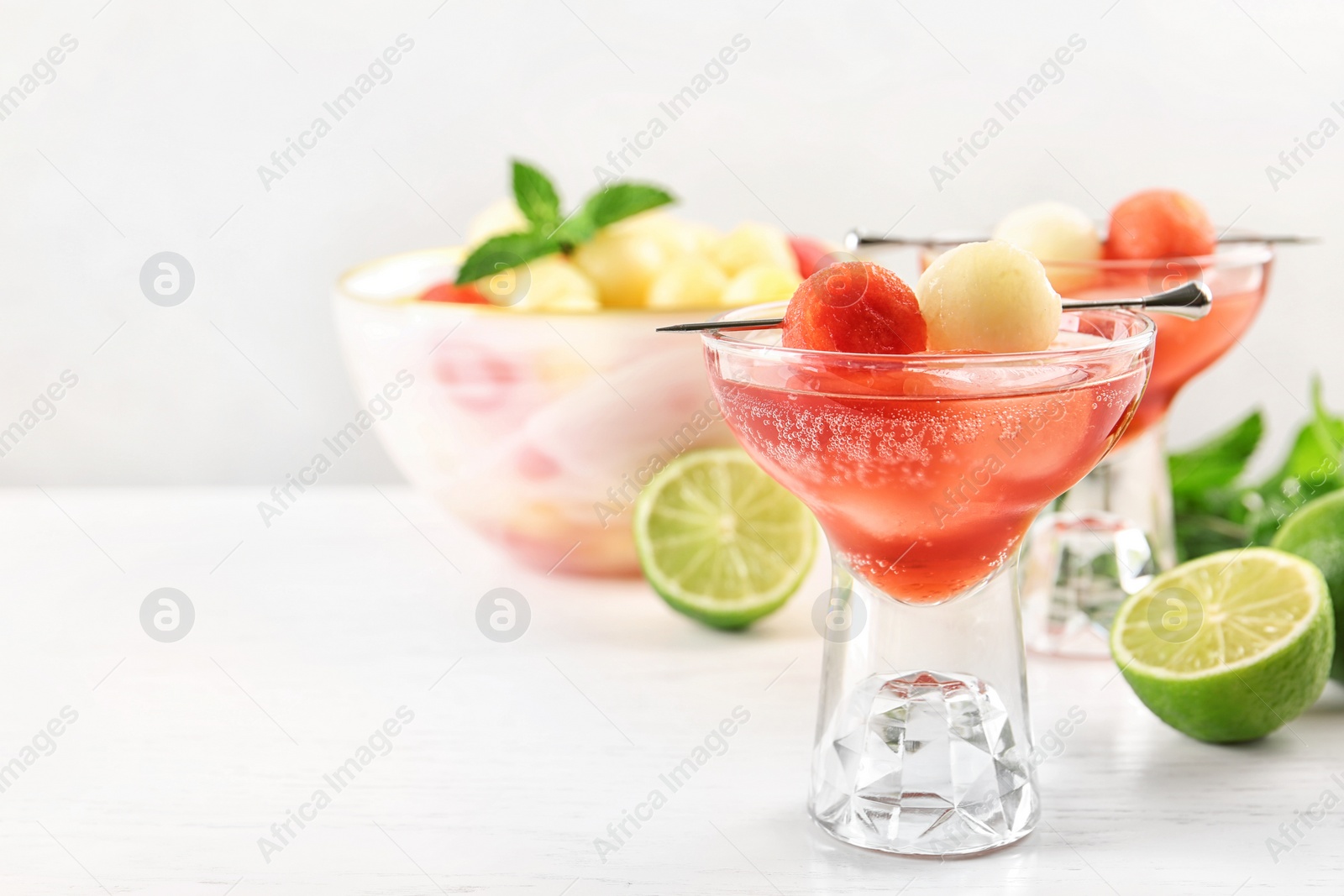 Photo of Glass of melon and watermelon ball cocktail on white wooden table. Space for text