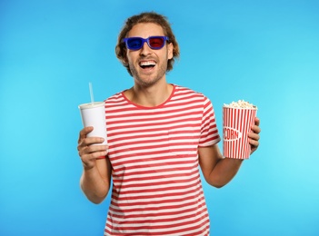 Photo of Man with 3D glasses, popcorn and beverage during cinema show on color background