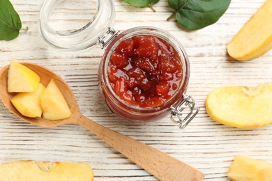 Photo of Delicious quince jam, fruits, leaves and spoon on white wooden table, flat lay