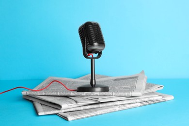 Newspapers and vintage microphone on light blue background. Journalist's work