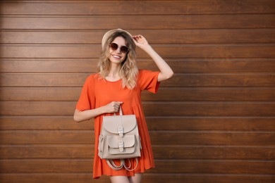 Photo of Young woman with stylish backpack near wooden wall