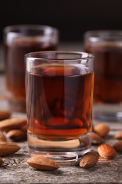 Photo of Shot glass with tasty amaretto liqueur and almonds on wooden table, closeup