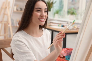 Photo of Beautiful young woman painting with brush in studio. Creative hobby