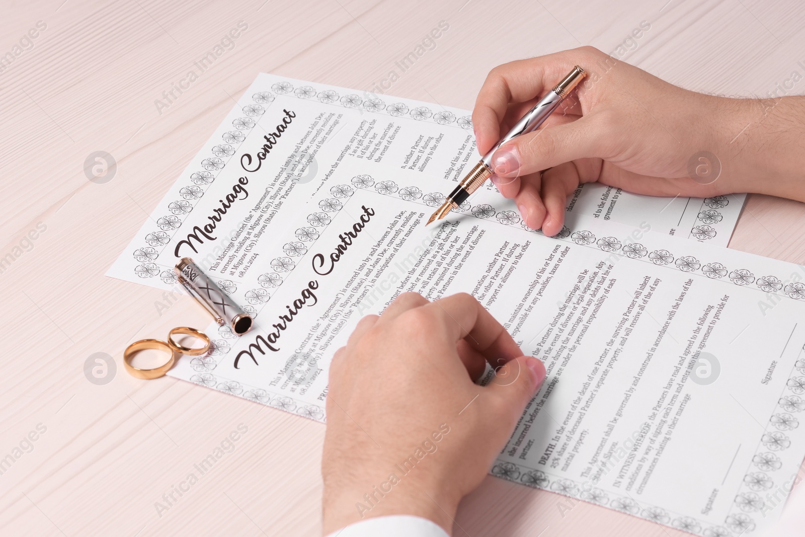 Photo of Man signing marriage contract at light wooden table, closeup