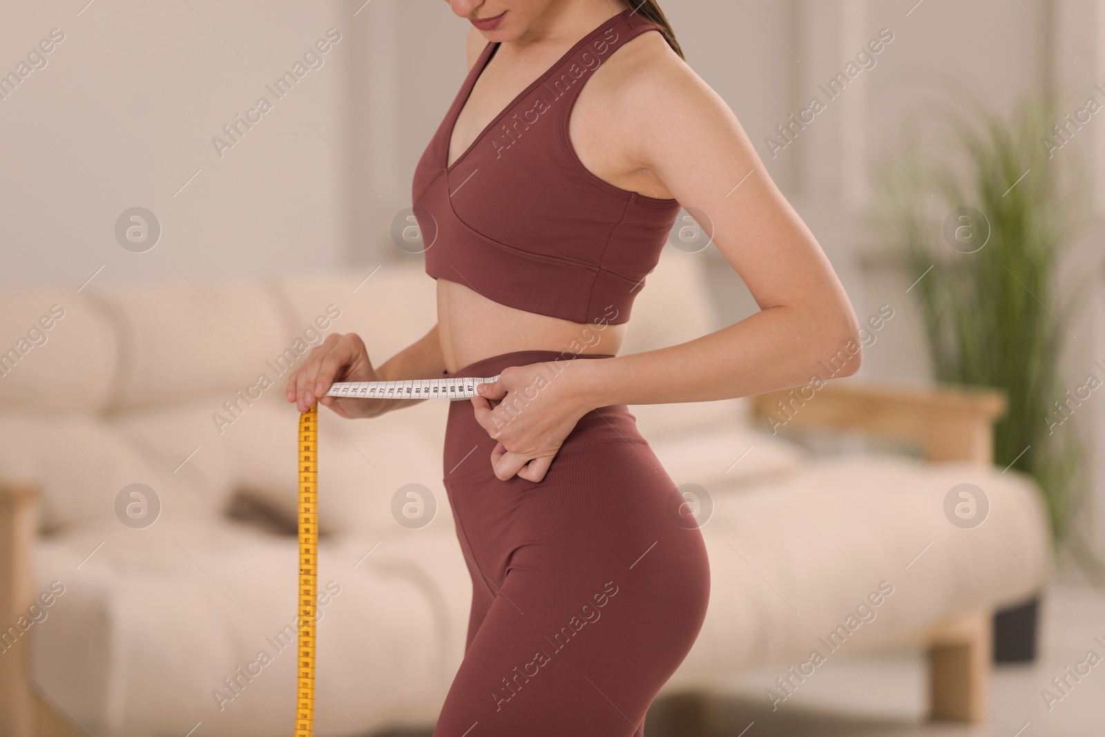 Photo of Woman in sportswear measuring waist with tape at home, closeup