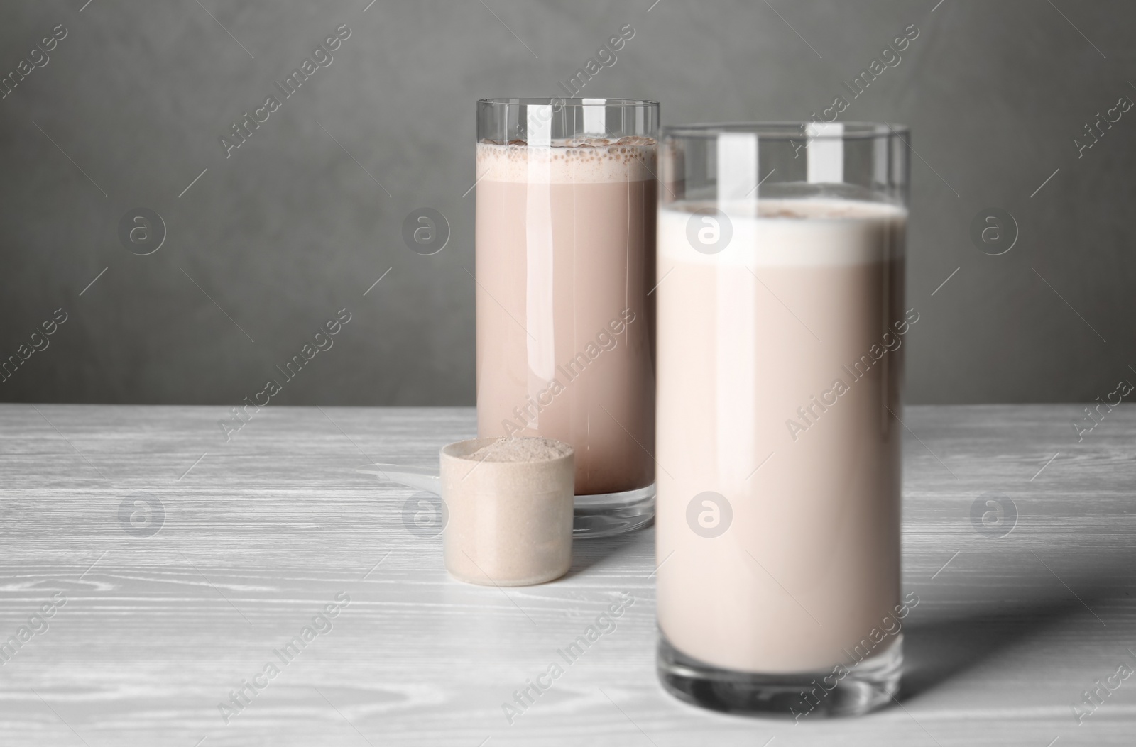 Photo of Glasses with protein shake and scoop of powder on white wooden table. Space for text