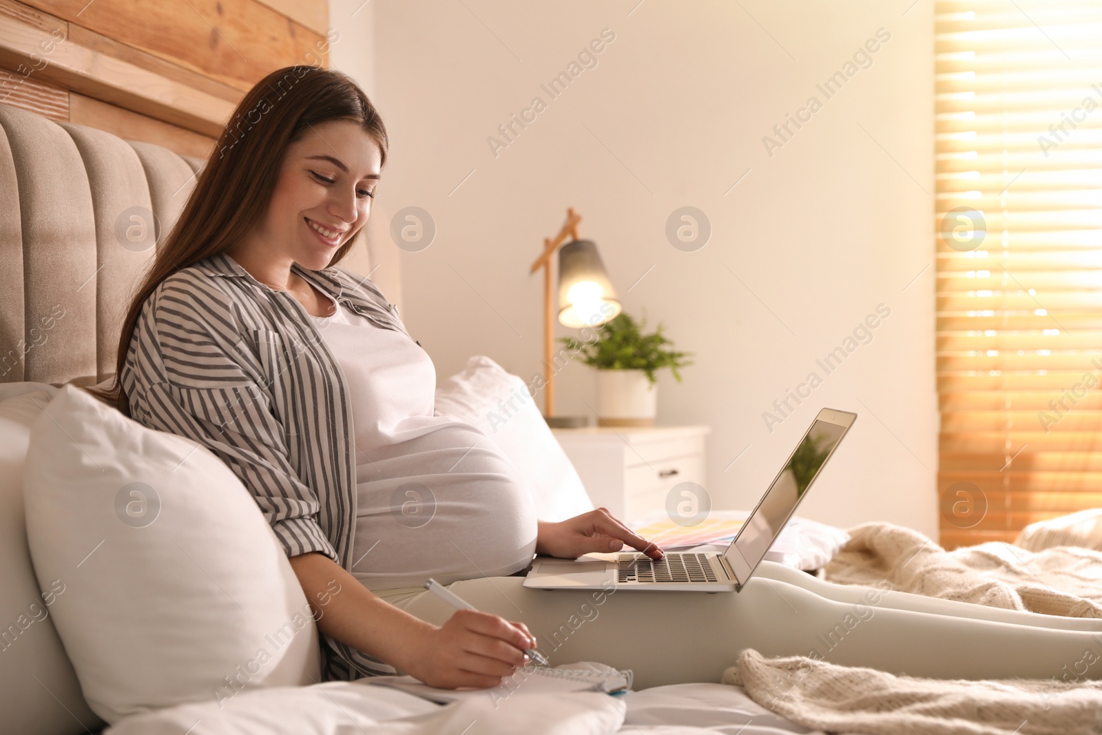 Photo of Pregnant woman working on bed at home. Maternity leave