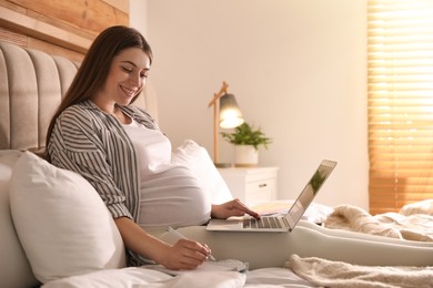 Photo of Pregnant woman working on bed at home. Maternity leave