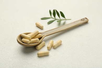 Photo of Vitamin capsules in spoon and leaves on white wooden table, closeup