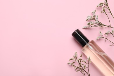 Bottle of baby oil and flowers on pink background, flat lay. Space for text