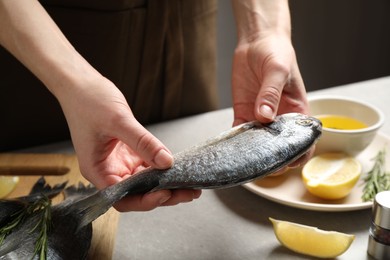 Photo of Woman holding dorada fish over grey table, closeup