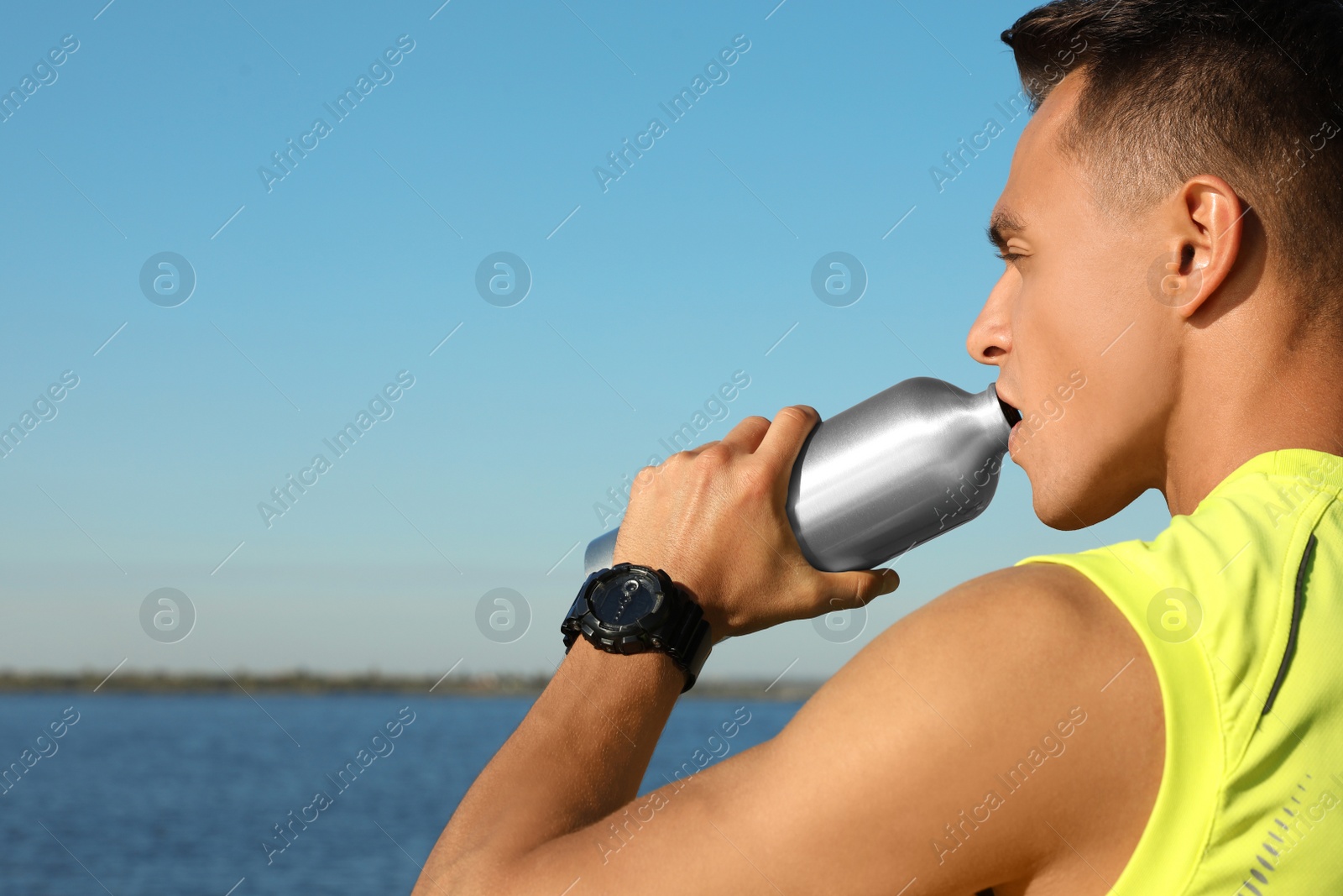 Photo of Young sporty man drinking from water bottle outdoors on sunny day. Space for text