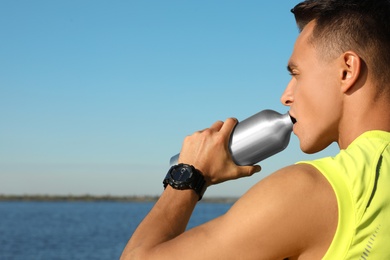 Young sporty man drinking from water bottle outdoors on sunny day. Space for text