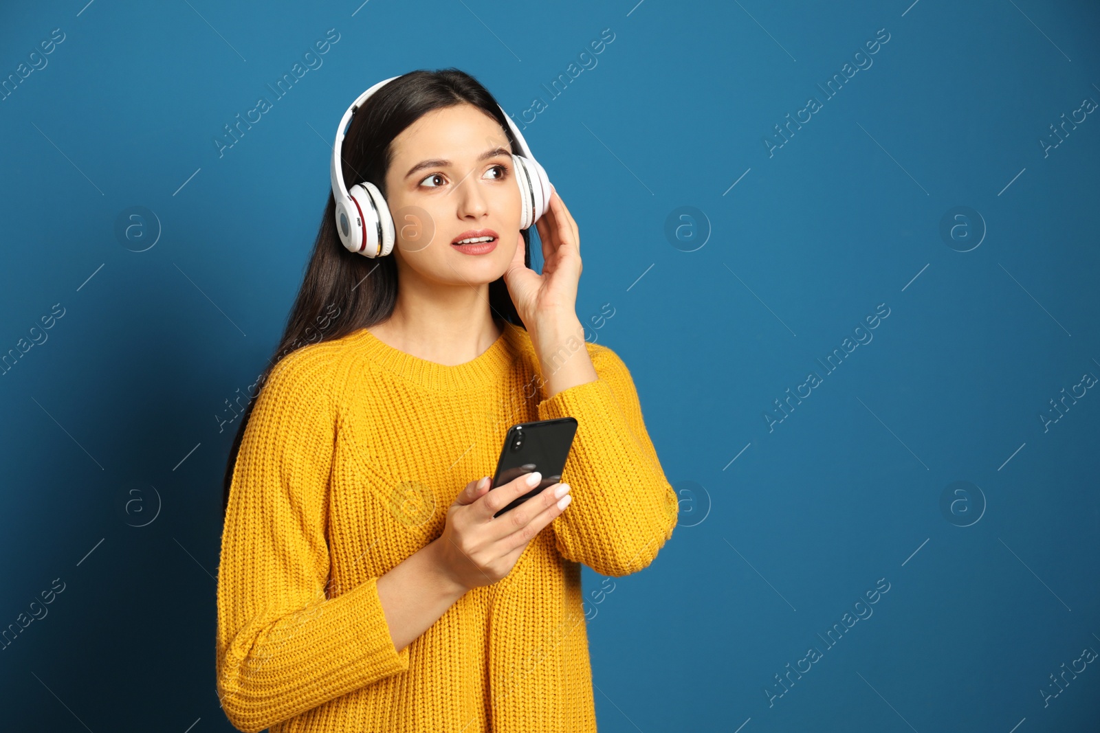 Photo of Young woman listening to audiobook on blue background. Space for text