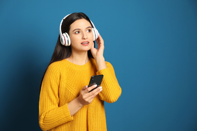 Young woman listening to audiobook on blue background. Space for text