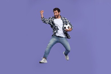 Photo of Emotional sports fan with soccer ball jumping on purple background