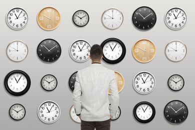 Image of Time management concept. Businessman standing in front of different clocks on light background, back view