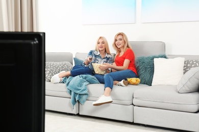 Photo of Young women with snacks watching TV on sofa at home