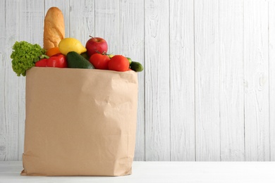 Photo of Shopping paper bag with different groceries on table against white wooden background. Space for text