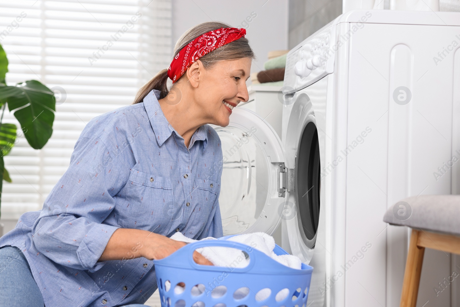 Photo of Happy housewife with laundry near washing machine at home