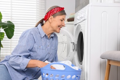 Happy housewife with laundry near washing machine at home