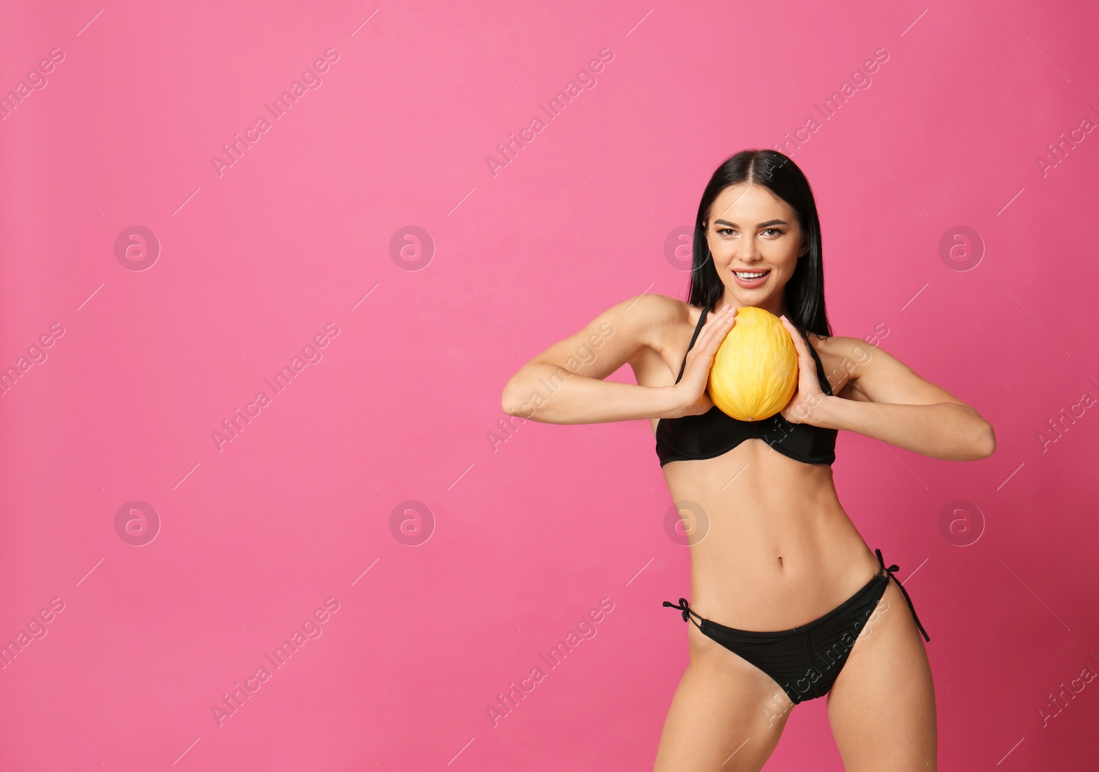 Photo of Beautiful young woman in black bikini with melon on pink background. Space for text