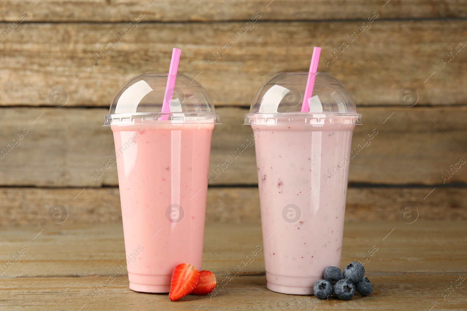 Photo of Plastic cups with different tasty smoothies and fresh fruits on wooden table