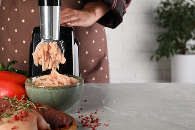 Photo of Woman making chicken mince with electric meat grinder at grey marble table indoors, closeup. Space for text
