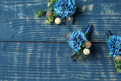 Photo of Stylish boutonnieres on blue wooden table, flat lay. Space for text