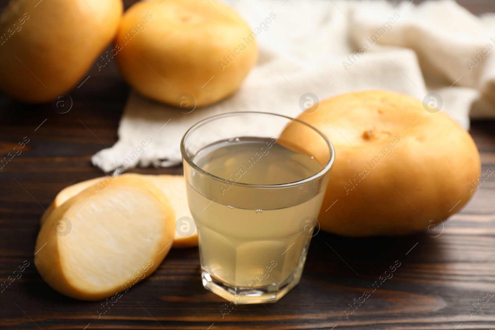 Photo of Glass of fresh natural turnip juice, cut and whole roots on wooden table