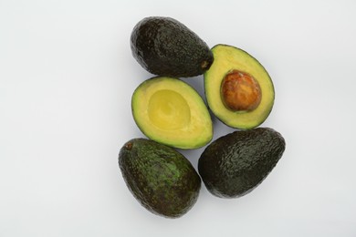 Tasty whole and cut avocados on white background, flat lay