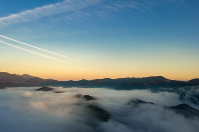 Image of Aerial view of beautiful mountains covered with fluffy clouds in morning. Drone photography