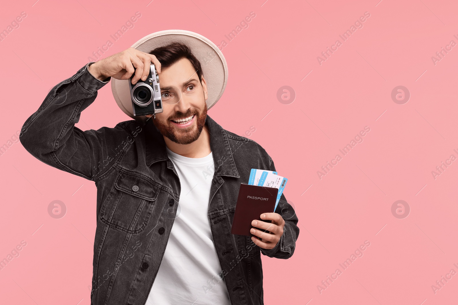 Photo of Smiling man with passport, tickets and camera on pink background. Space for text