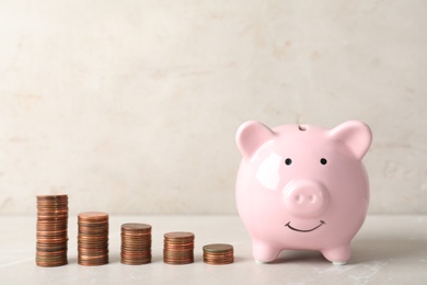 Ceramic piggy bank and many coins on table against light background. Space for text