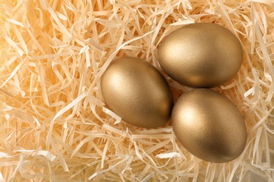 Photo of Three golden eggs in hay, top view. Space for text