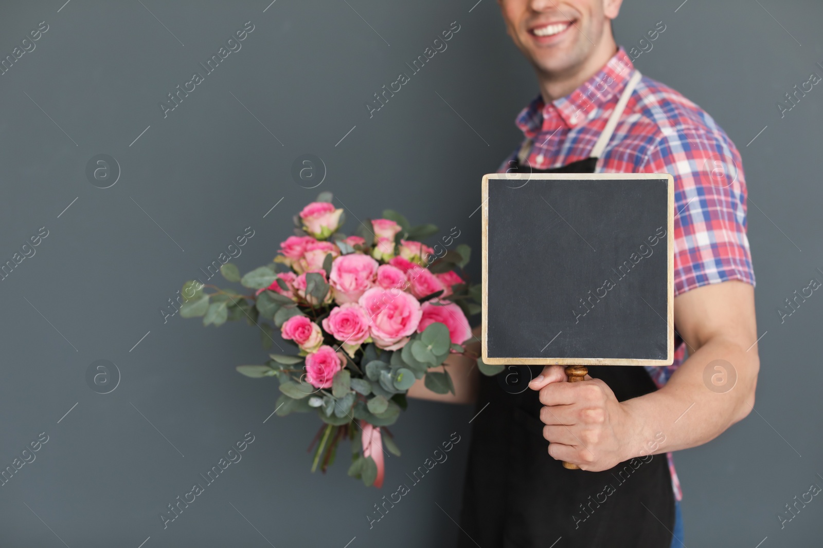 Photo of Male florist holding small chalkboard and bouquet on dark background