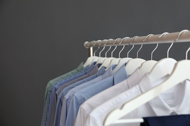 Photo of Wardrobe rack with men's clothes against grey background. Space for text